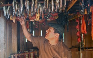 Jason Aceveda shows off hooligan, salmon and seal in the smokehouse at the Kake culture camp. Photo by Erik Neumann, KCAW - Sitka.