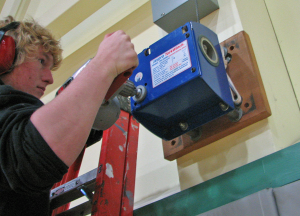 Sitka senior Thor Becker tests out a special drill bit to raise the gym's basketball hoops. Photo by Robert Woolsey, KCAW - Sitka.