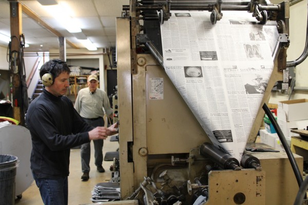 James Poulson and his father Thad operate the printing press, which is the same piece equipment used by the family to print the paper in 1969. James was four years old then and has since become the staff photographer. (Emily Kwong/KCAW photo)