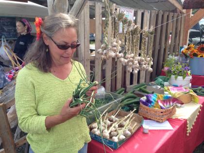 Lori Jenkins of Synergy Gardens holds garlic scapes her WWOOFers helped harvest - Photo by Shady Grove Oliver/KBBI