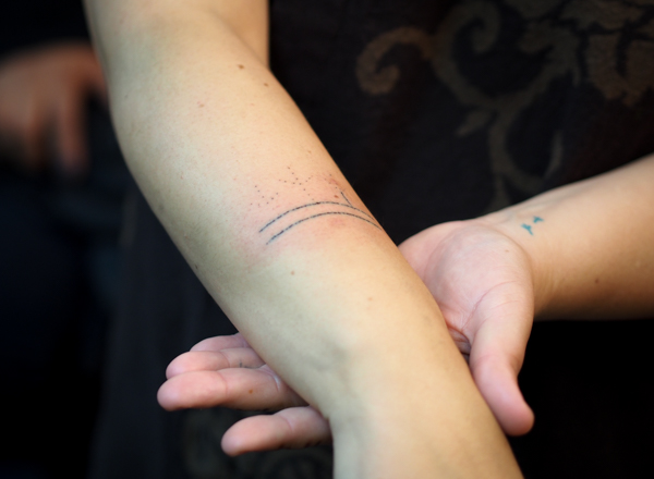 Holly Mititquq Nordlum shows off her partially complete tattoo during a live demonstration at Anchorage's Above The Rest studio. Each horizontal line is 40 individual stitch marks through the first layer of skin. Before starting the stitches, Jacobsen poked the basic design of three bird feet rising from the lines. Nordlum's Inupiaq name, Mititquq, means a place where birds land, and she commemorates achieving big life goals with bird feet tattoos, like the two on her opposite wrist, done with a tattoo gun. (Photo: Zachariah Hughes, KSKA)