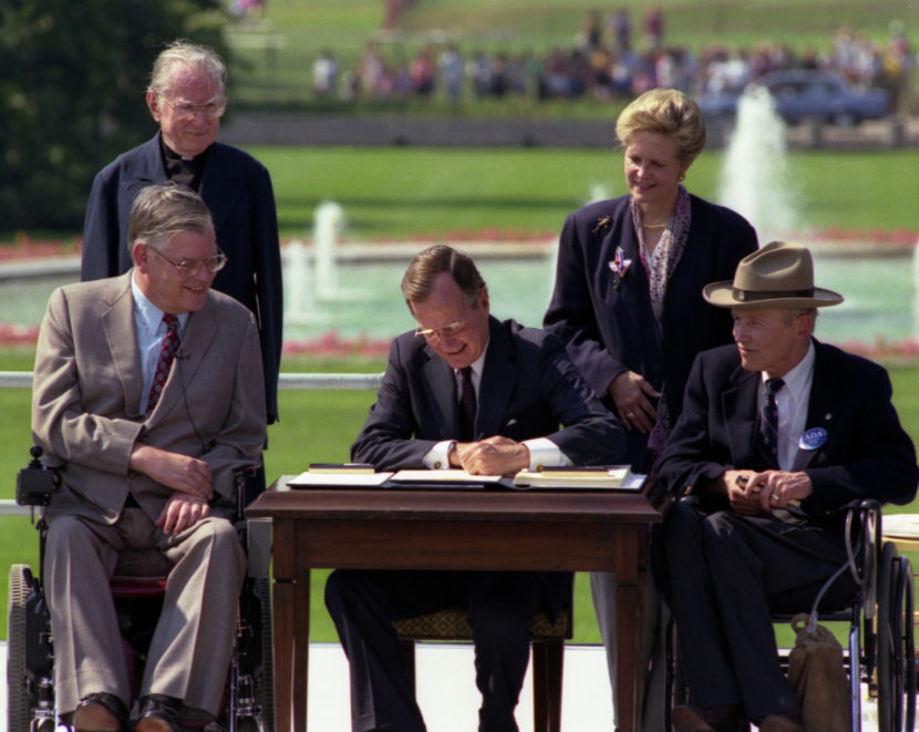P14777-18  President Bush signs the Americans with Disabilities Act on the South Lawn of the White House.  Sharing the dais with the President and he signs the Act are (standing left to right):  Rev. Harold Wilkie of Clairmont, California; Sandra Parrino, National Council on Disability; (seated left to right):  Evan Kemp, Chairman, Equal Opportunity Commission; and Justin Dart, Presidential Commission on Employment of People with Disabilities.  Mrs. Bush and Vice President Quayle participate in the Ceremony. 26 July 1990 (Photo courtesy of George Bush Presidential Library and Museum)