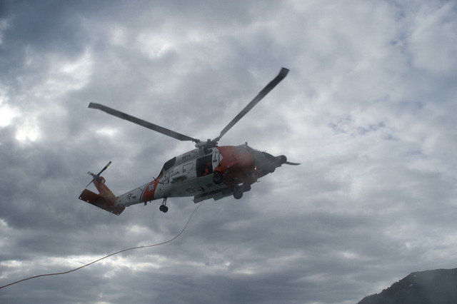 A white and grey coast guard helicopter over cloudy skies