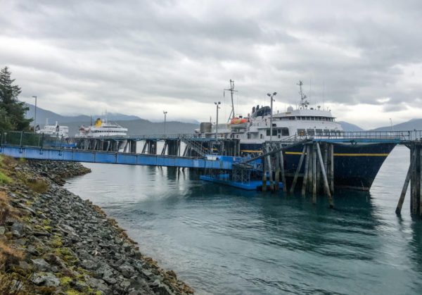 A blue ferry with a white cabin sits at dock next to a causeway
