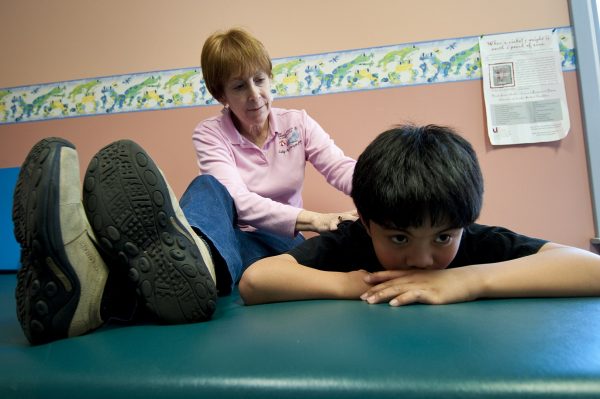 Occupational therapist sitting beside young child participating in physical therapy