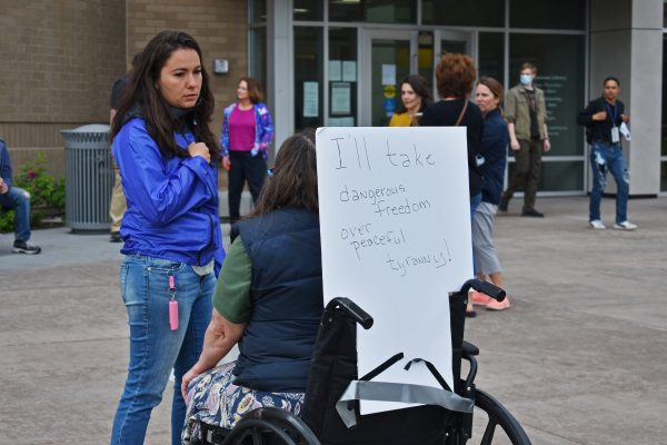 A woman speaks to someone in a wheelchair. On the back of the wheelchair is a sign that reads, "I'll take dangerous freedom over peaceful tyranny!"