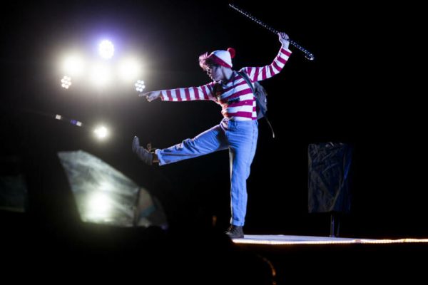 A person dressed like Where's Waldo dances on stage in front of bright lights