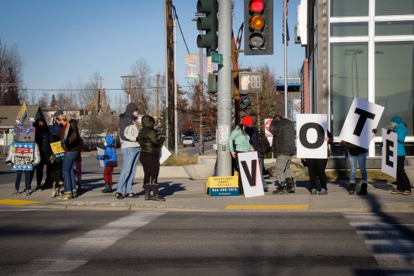 people stand on a street corner with "VOTE" signs