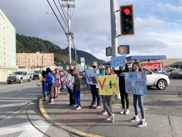 A group of sixth-graders hold signs on a street corner with messages that read "Vote" and "Thank you for voting."