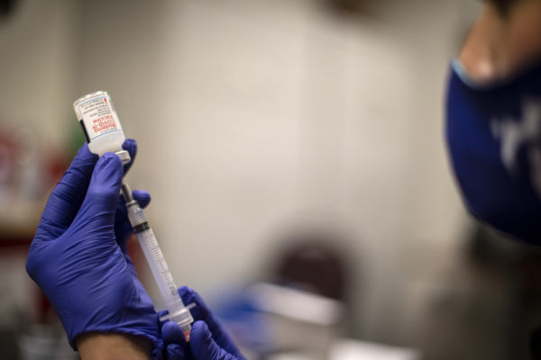 A man in medical gloves pulls out vaccine from a vial