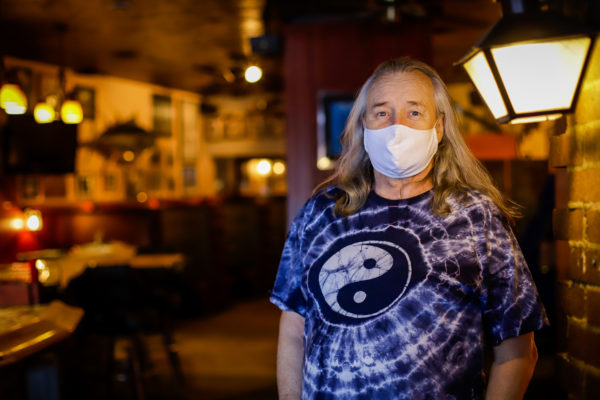 A man in a tie-dye shirt poses for a photo. He's wearing a face mask.