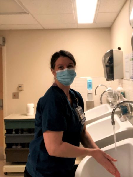 A woman in a face mask and scrubs washes her hands.