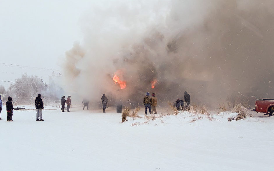 Peoplpe gather around a burning building in a snowy area