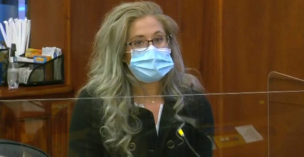 A woman in a blue surgical mask speaks on a microphone