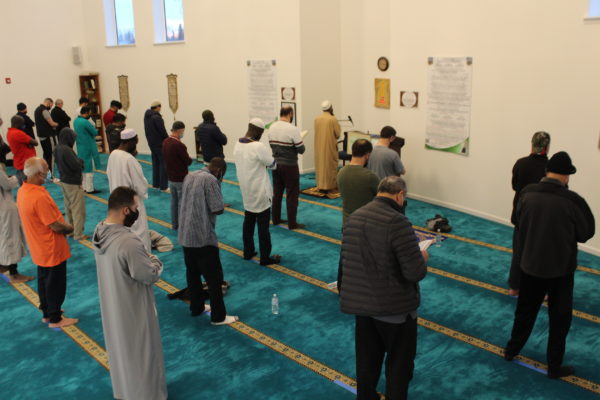 Men stand with their heads bowed on rows in a turqoise carpet