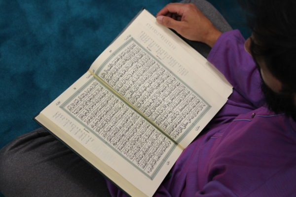 A man dressed in purple reads through a book with arabic script