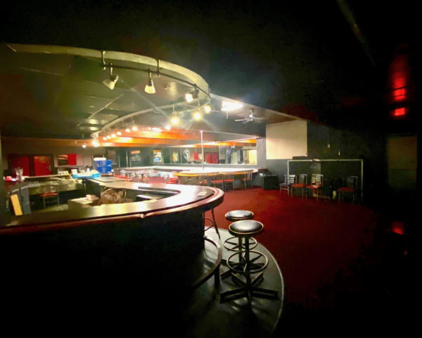 A dark room with some bar stools near a rounded bar