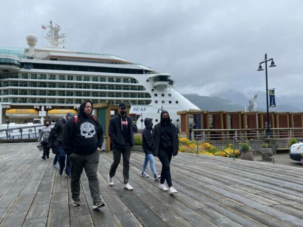 People walk on a dock, with a cruise ship in the background.