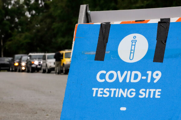cars lined up and a sign that reads "COVID-19 TESTING SITE"
