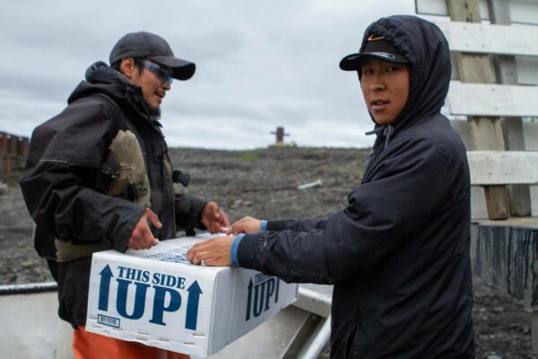 Two men in jackets lift a box that says "This side up"