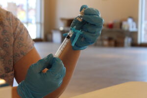 A person wearing blue gloves draws liquid from a vial into a syringe