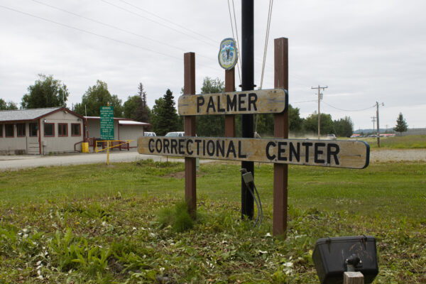 A wooden sign in a grassy field next to a dirt road that says Palmer Correctional Center