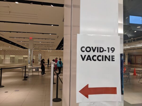 A white paper sign that says "COVID-19 vaccine" with an arrow pointing into a large white room