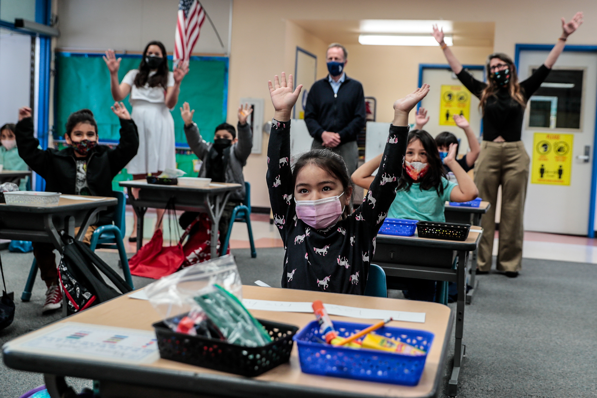 Children in a classroom with face masks put their hands in the air.