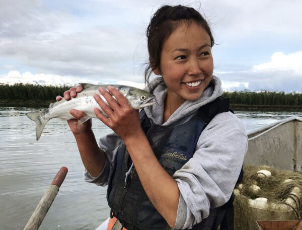 A smiling girl next to a river holding a fish.