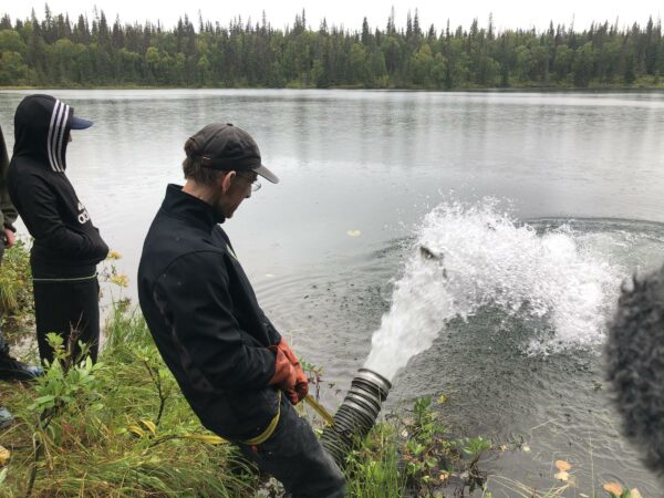 A man holds a hose as water shoots out of it into a lake.
