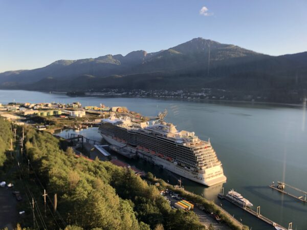 A cruise ship docked, with a mountainous backdrop, on a sunny day.