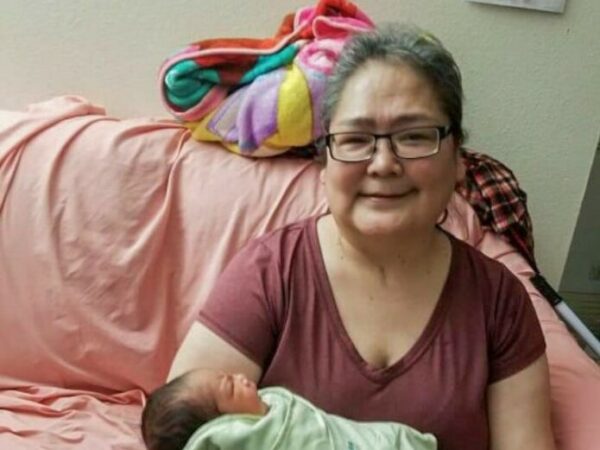 A woman sits on a bed holding a baby.