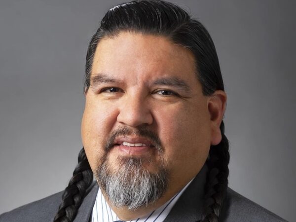 The portrait of a man in braids and a goatee, wearing a suit.