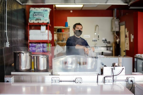 A man in a mask stands at a restaurant's kitchen.
