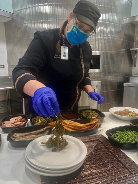 A woman in a chef uniform and wearing gloves plates pickled fiddlehead ferns.