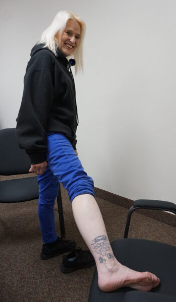 A woman roles up her pant leg to show a tattoo.