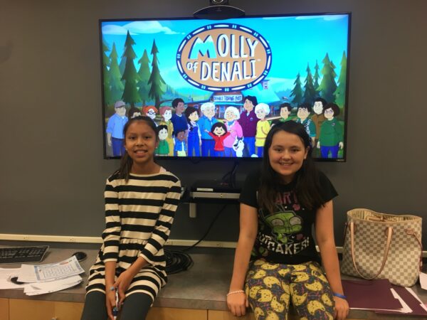 Two girls are sitting in front of a TV that says "Molly of Denali."