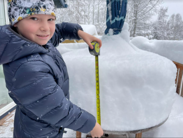 A girl holds a tape measure to some snow on a table