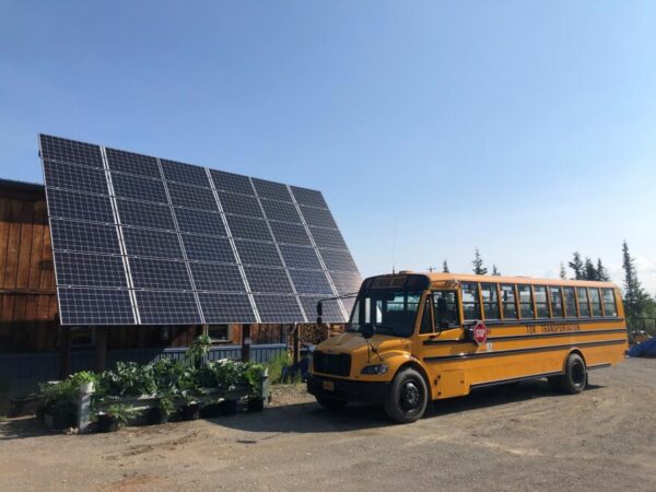 A school bus is parked next to a big solar panel.
