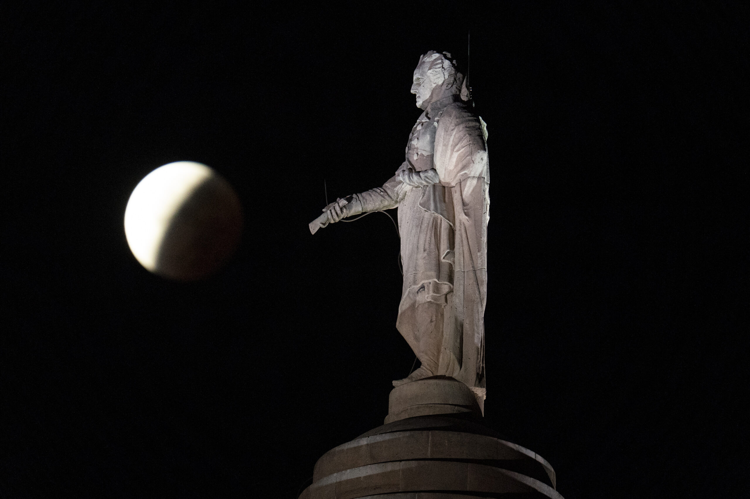 A moon behind a statute.