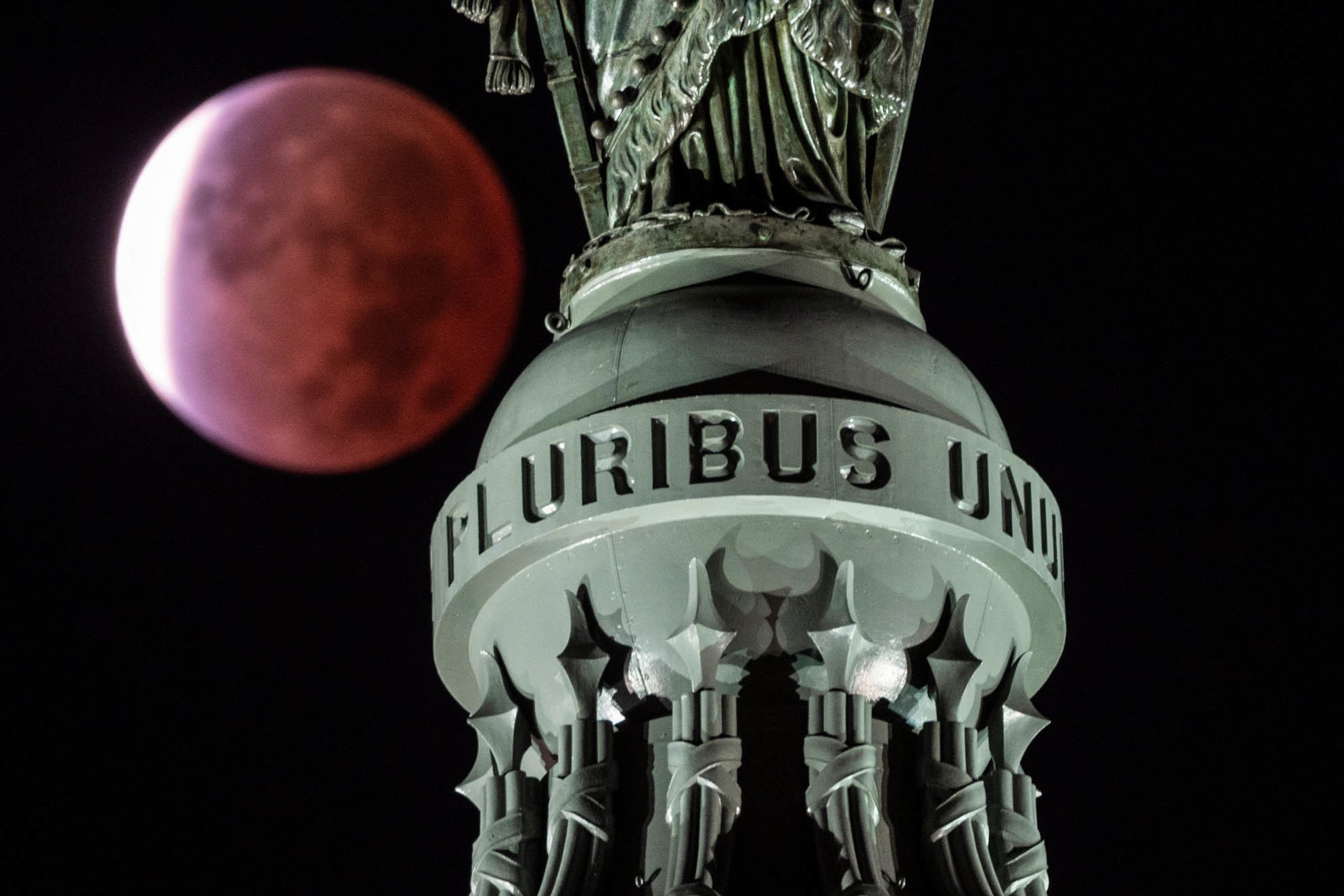 A red moon behind a statute.