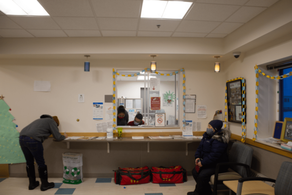 A couple people wait in the lobby of a health care clinic, wearing masks.