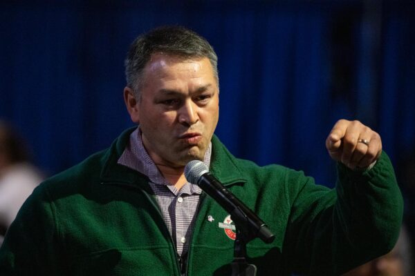 A man in a green jacket talks into a microphone.
