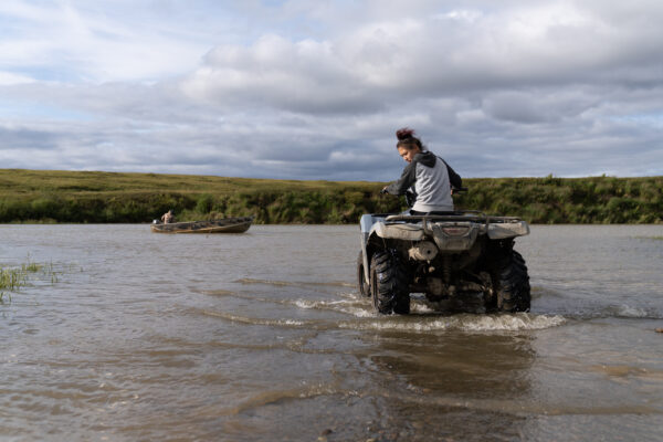 A woman rides her ATV through the water.