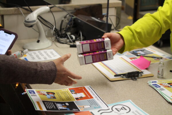 A person reaches for two small purple boxes from the hand of another person