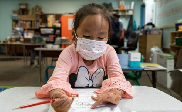 A young girl in a face mask writes her name.