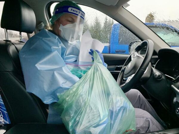 A woman in full PPE has her hand in a plastic bag in the car.