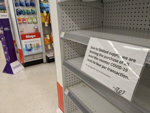 Empty shelves with a sign that says "due to limited supply, we are limiting the purchase of all over the counter covid-19 tests to four per transaction"