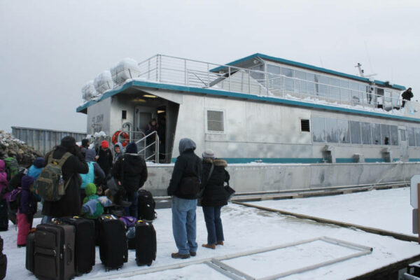 People stand outside of a boat in a line, in the snow.