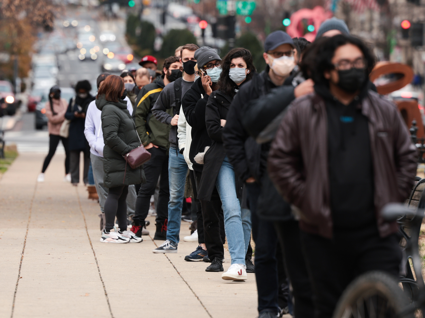 A lone line of people with masks on outside.